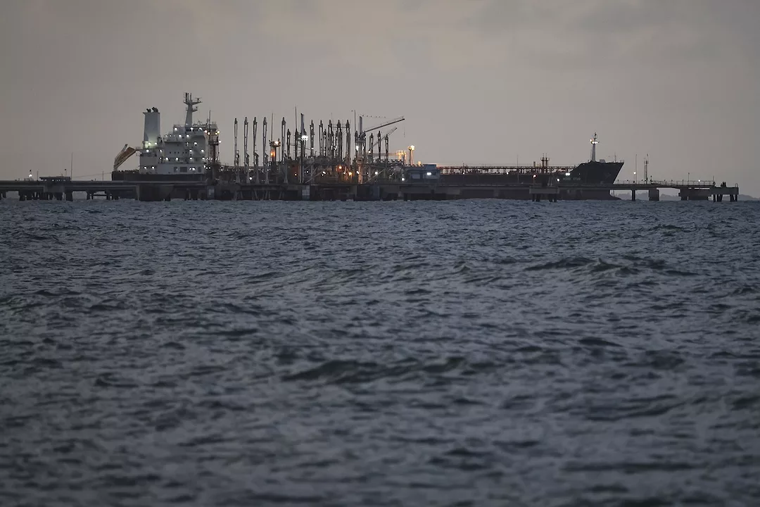 A grey container ship docked in choppy waters on a cloudy day