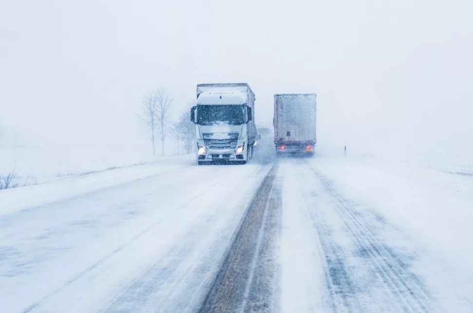 TWO SNOW-COVERED TRUCKS PASS EACH OTHER ON AN ICY HIGHWAY