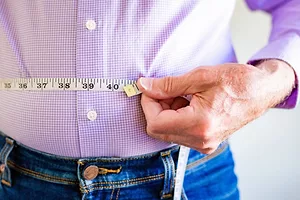 A CLOSE UP VIEW OF A MAN MEASURING HIS WAIST WITH A MEASURING TAPE AT MORE THAN FORTY INCHES