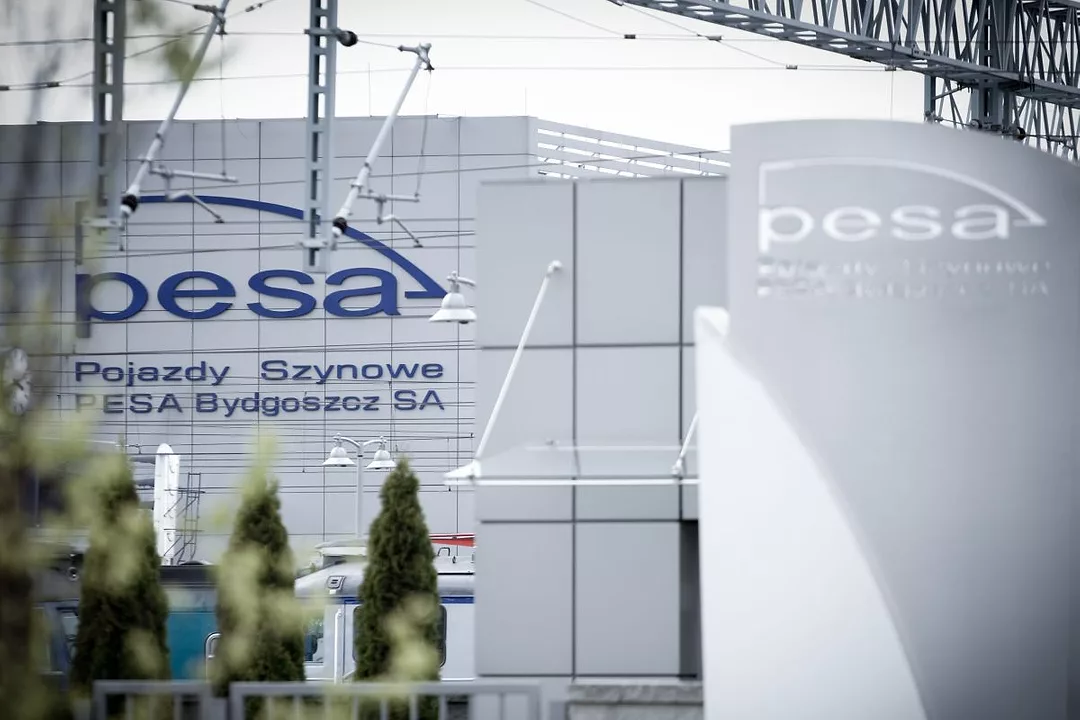 OVERHEAD TRAIN INFRASTRUCTURE FRAMES A COMMERCIAL BUILDING BEARING THE NAME PESA