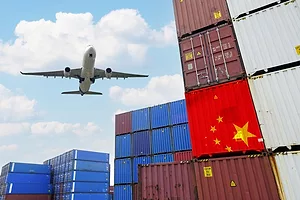 A CARGO PLANE FLIES OVER A STACK OF CONTAINERS, ONE OF THEM BEARING THE FLAG OF CHINA
