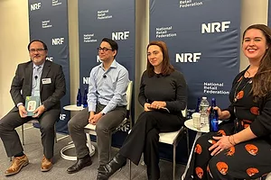 TWO WOMEN AND TWO MEN SIT ON A STAGE IN FRONT OF NRF BANNERS