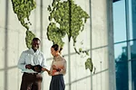 GLOBAL BUSINESS TRADE PROCUREMENT iStock-Noko LTD-2220160472.jpg TWO BUSINESS COLLEAGUES DISCUSS A DOCUMENT IN FRONT OF A MAP OF THE WORLD