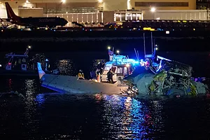 A crashed plane in the water at night, being recovered by a rescue boat