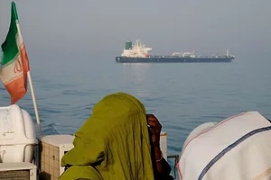 FIGURES WITH HEAD COVERINGS IN FRONT OF A FLAG LOOK OUT AT A SHIP IN THE SEA