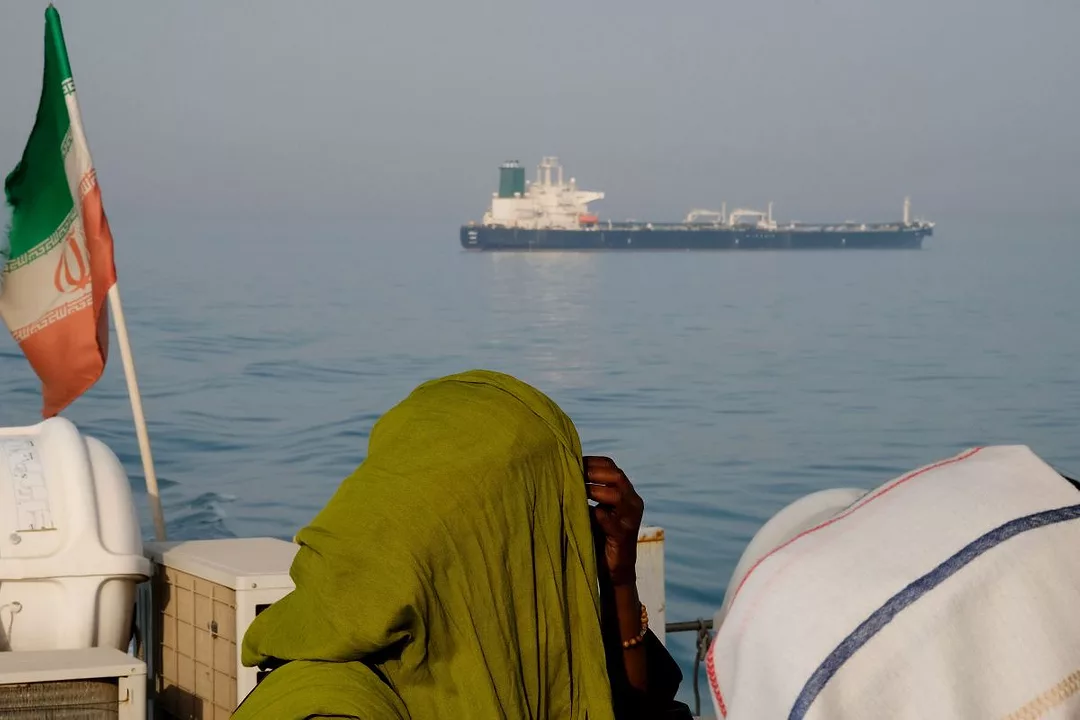 FIGURES WITH HEAD COVERINGS IN FRONT OF A FLAG LOOK OUT AT A SHIP IN THE SEA