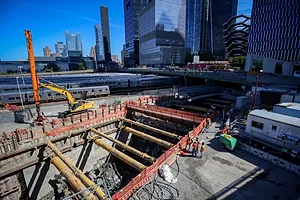 A HOLE IN THE GROUND FOR CONSTRUCTION WITH SKYSCRAPERS VISIBLE IN THE BACKGROUND