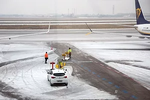 WORKERS IN HI-VIS VESTS CONFER ON A SNOW COVERED RUNWAY