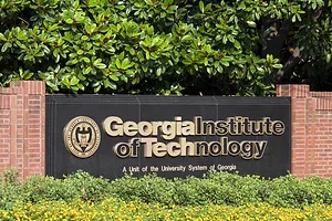 A large black plaque that reads "Georgia Institute of Technology" connected by a brick wall on either side and surrounded by trees and shrubs