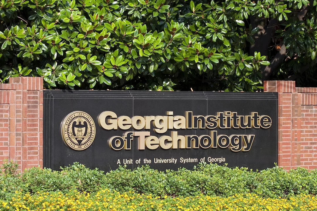 A large black plaque that reads "Georgia Institute of Technology" connected by a brick wall on either side and surrounded by trees and shrubs