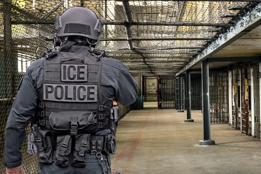 AN ICE POLICE OFFICER IN COMBAT GEAR WALKS DOWN THE CORRIDOR OF A MASSIVE JAIL