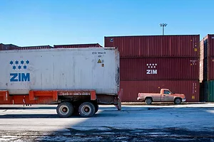 A TRUCK CARRIES A CONTAINER LABELED ZIM PAST OTHER CONTAINERS LABELED ZIM