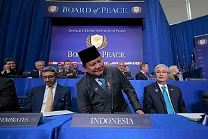 A MAN IN A SQUARE HAT STANDS AT A PODIUM IN A CONFERENCE WITH OTHERS