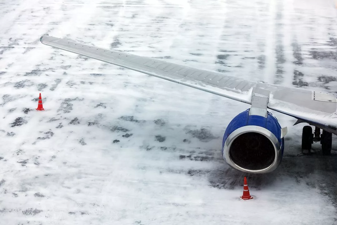 AN AIRCRAFT SITS ON A SNOWY RUNWAY, SURROUNDED BY HAZARD CONES