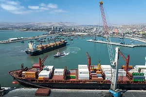 A container ship docked beneath a tall white crane along a concrete shoreline