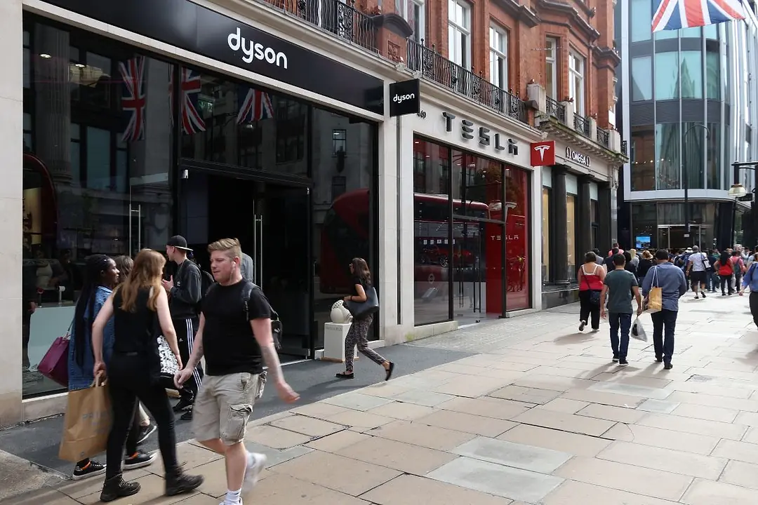 PEOPLE WALK PAST A STORE FRONT, A BRITISH FLAG HANGING ABOVE