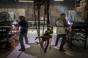 TWO WELDERS WORK AT BENCHES, SPARKS FLYING