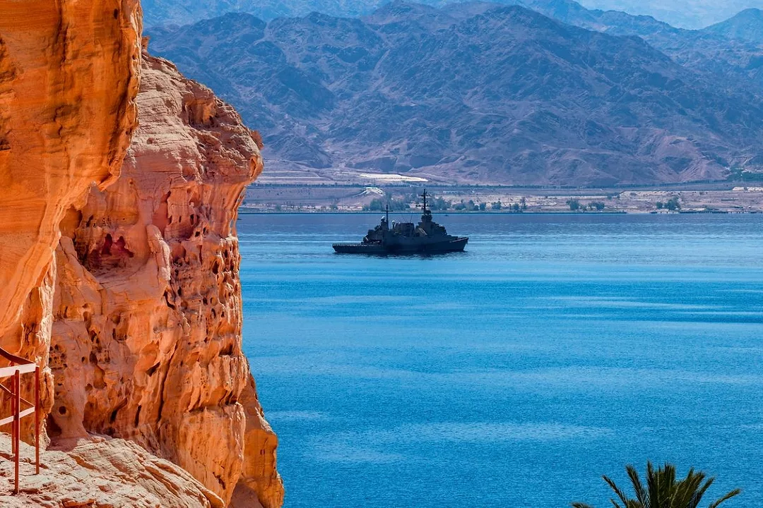 A MILITARY SHIP AT SEA IS FRAMED BY RED STONE CLIFFS