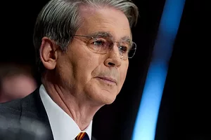 A MAN WITH GREYING HAIR IN SPECTACLES WEARING A JACKET AND TIE FACES SIDE ON TO THE CAMERA
