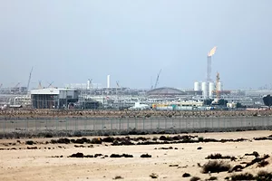 AN INDUSTRIAL PLANT WITH A CHIMNEY BLOWING FLAME SITS IN THE DESERT