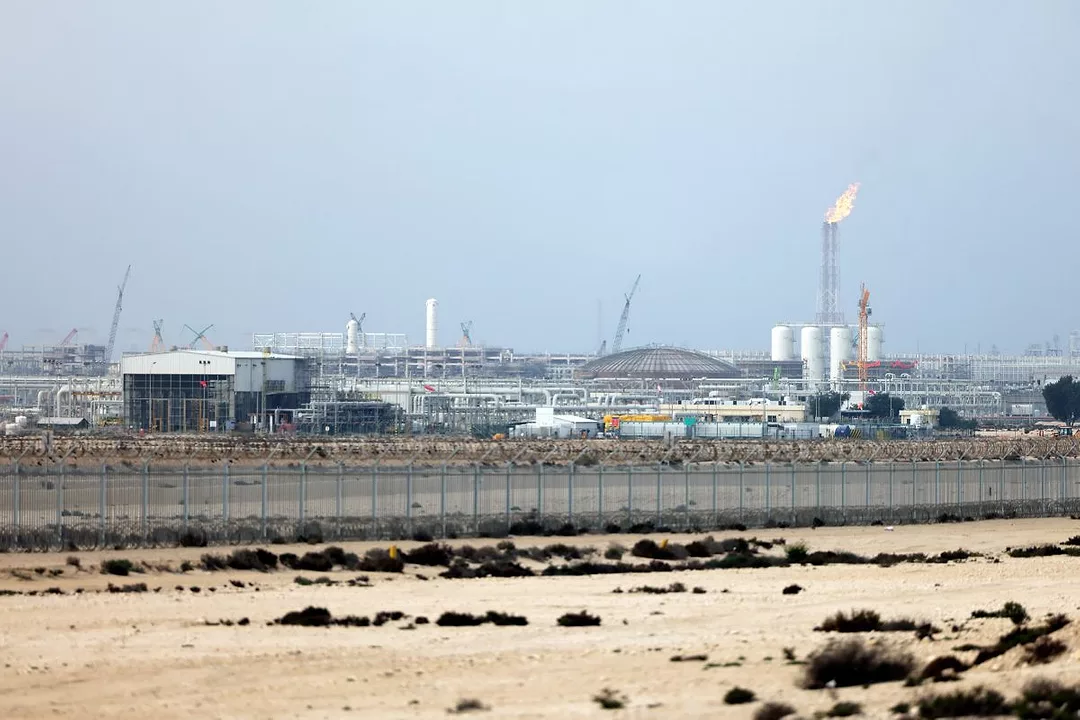 AN INDUSTRIAL PLANT WITH A CHIMNEY BLOWING FLAME SITS IN THE DESERT
