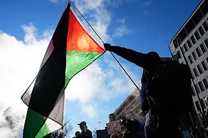 A man holding an Iranian flag on a sunny day, surrounded by protesters