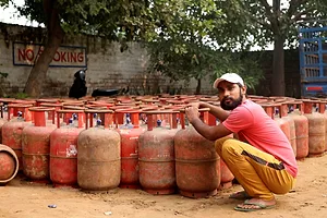 A WORKER SQUATS HOLDING AN ORANGE LNG CANISTER, IN A COURTYARD FULL OF DOZENS OF CANISTERS