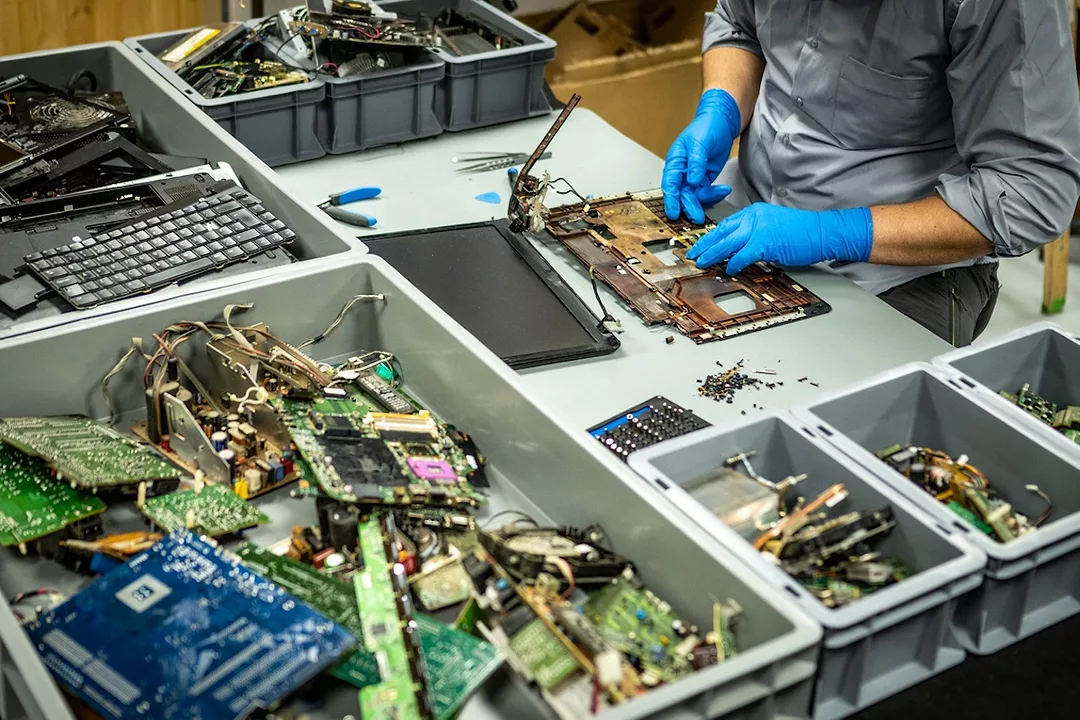 A man in rubber gloves standing at a table full of various electronic parts