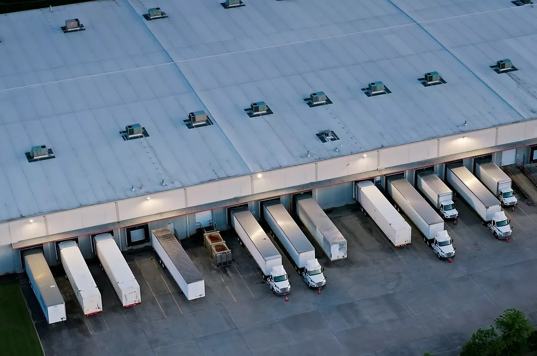AN AERIAL SHOT OF A WAREHOUSE WITH MULTIPLE TRUCKS PARKED AT LOADING BAYS