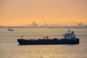 A TANKER AT SEA AT SUNSET, CRANES IN THE BACKGROUND ON LAND