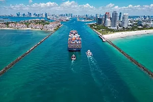 A container ship moving through a narrow waterway that feeds into a cityscape on a sunny day