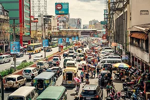 A busy city street filled with cars, flanked by bright blue roadsigns and green and tan buildings