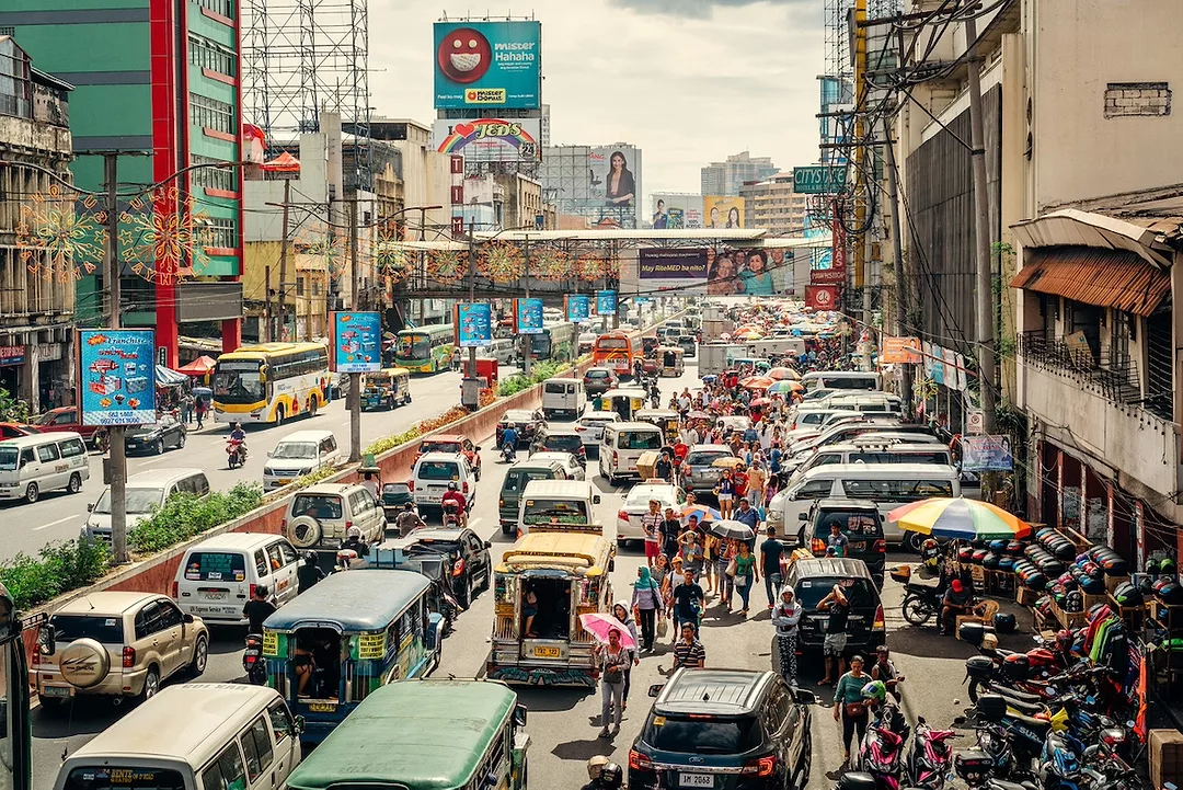 A busy city street filled with cars, flanked by bright blue roadsigns and green and tan buildings
