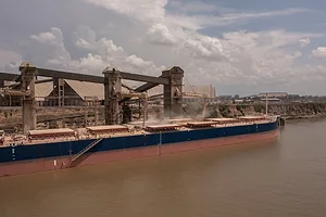 A long blue and red container ship being loaded with grain at a port on a cloudy day