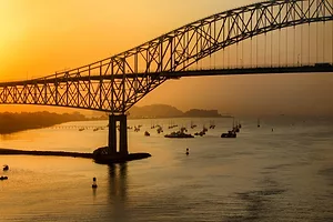 A tall metal bridge over the Panama Canal at sunset