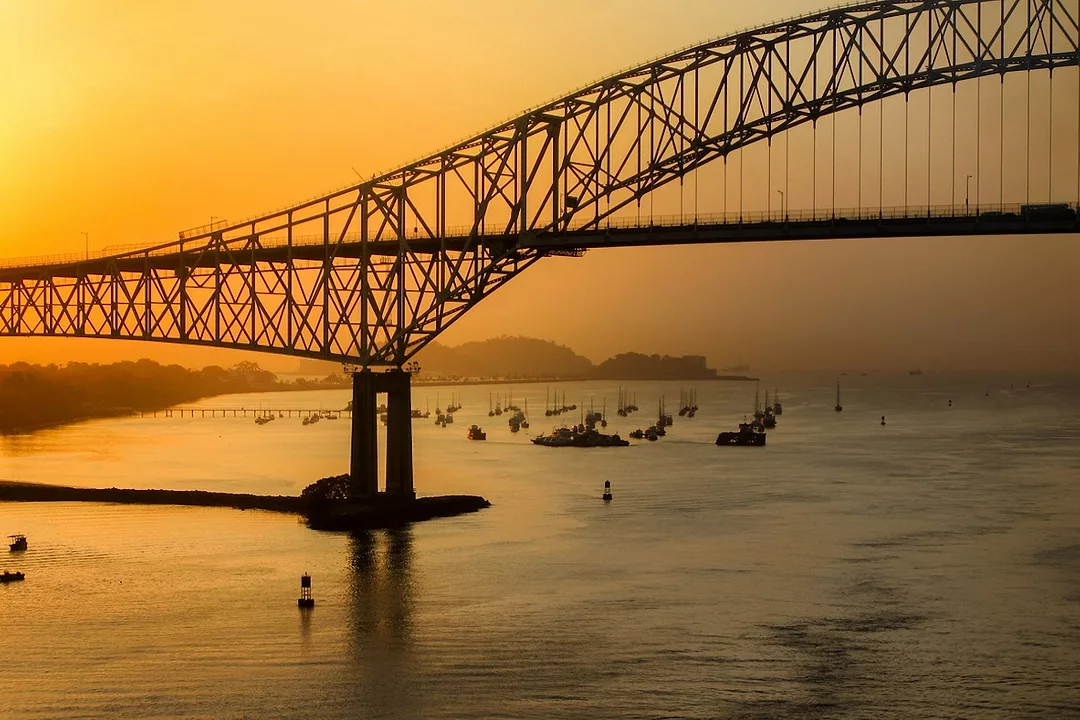 A tall metal bridge over the Panama Canal at sunset