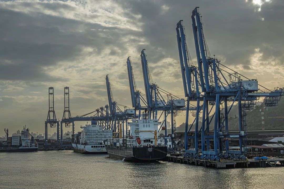 A PORT IS SEEN FROM THE WATER, WITH MULTIPLE CRANES TOWERING OVER DOCKED SHIPS
