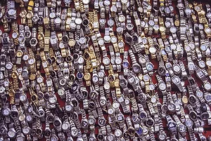 A LARGE SPREAD OF WATCHES LIES ON A VENDOR'S TABLE