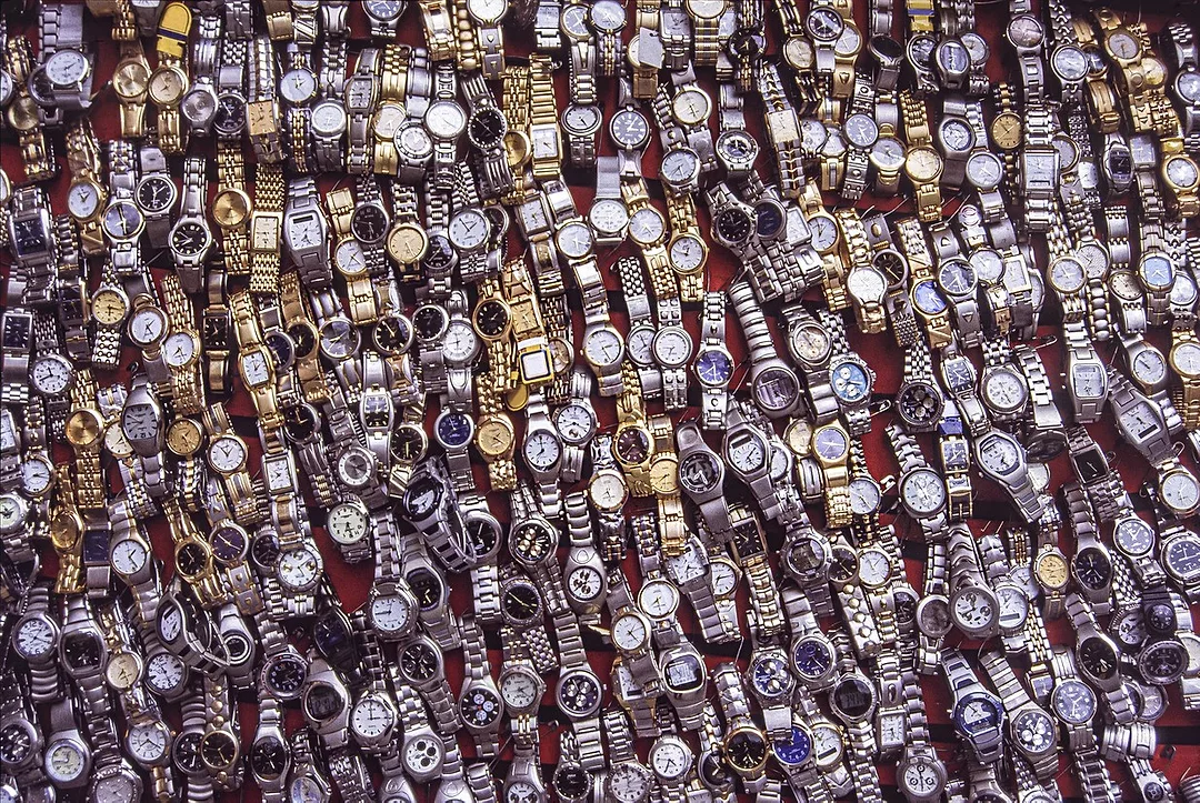 A LARGE SPREAD OF WATCHES LIES ON A VENDOR'S TABLE