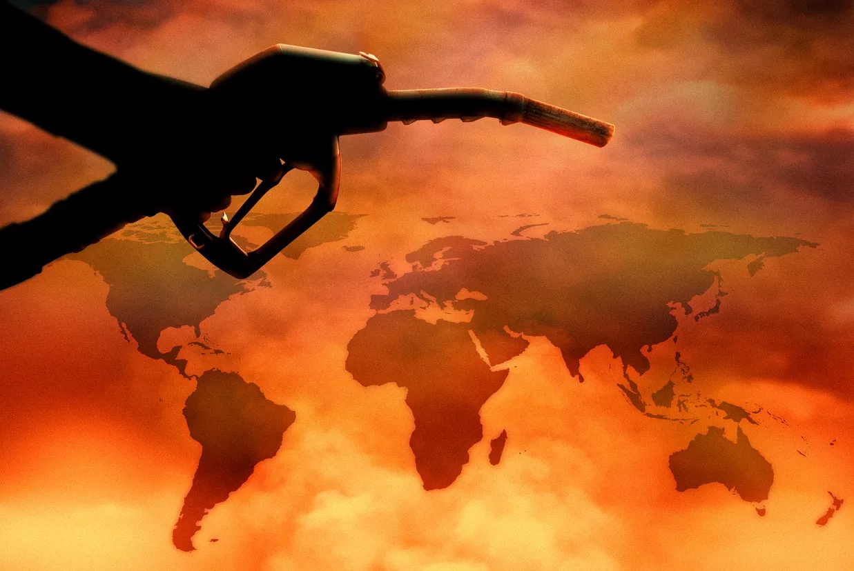 A hand holds a fuel pump over a map of the world. 