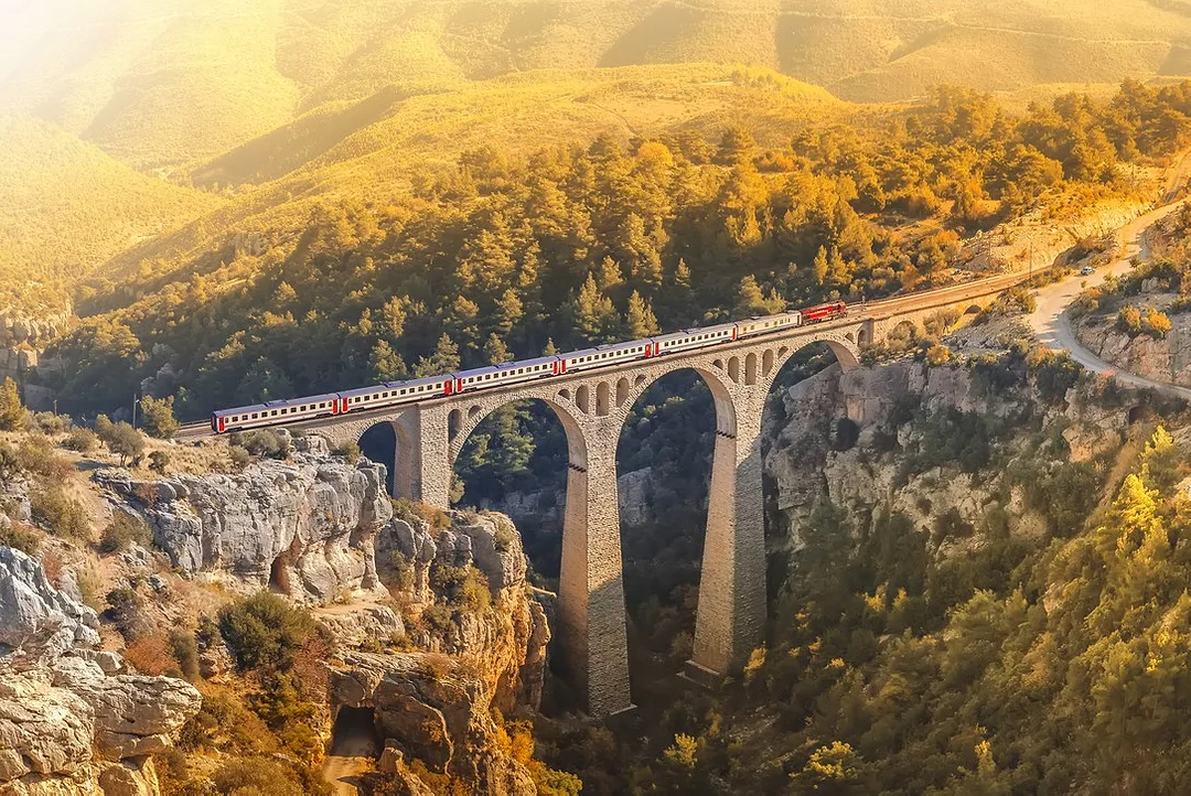 A TRAIN CROSSES A DRAMATIC VIADUCT BRIDGE OVER A VALLEY AT SUNSET