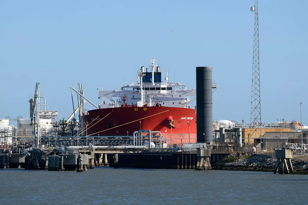 A LARGE RED TANKER SITS AT DOCK SURROUNDED BY CRANES