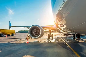 A PLANE SITS ON THE TARMAC, CONNECTED TO A FUEL LINE, THE SUN SETTING IN THE DISTANCE