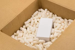 AN OPEN SHIPPING BOX SHOWS A TINY BOXED ITEM IN A SEA OF PACKING PEANUTS