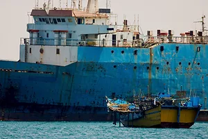 A large blue cargo ship being approached by a small yellow boat