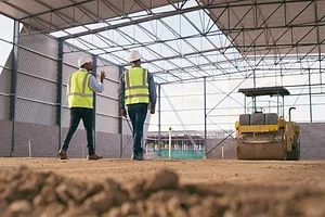 Two men in yellow safety vests and helmets walking under a half-built warehouse facility