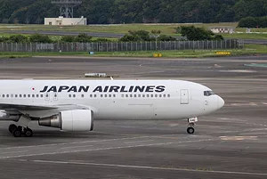 A white airplane on a runway that reads "JAPAN AIRLINES" in navy blue lettering along the side.