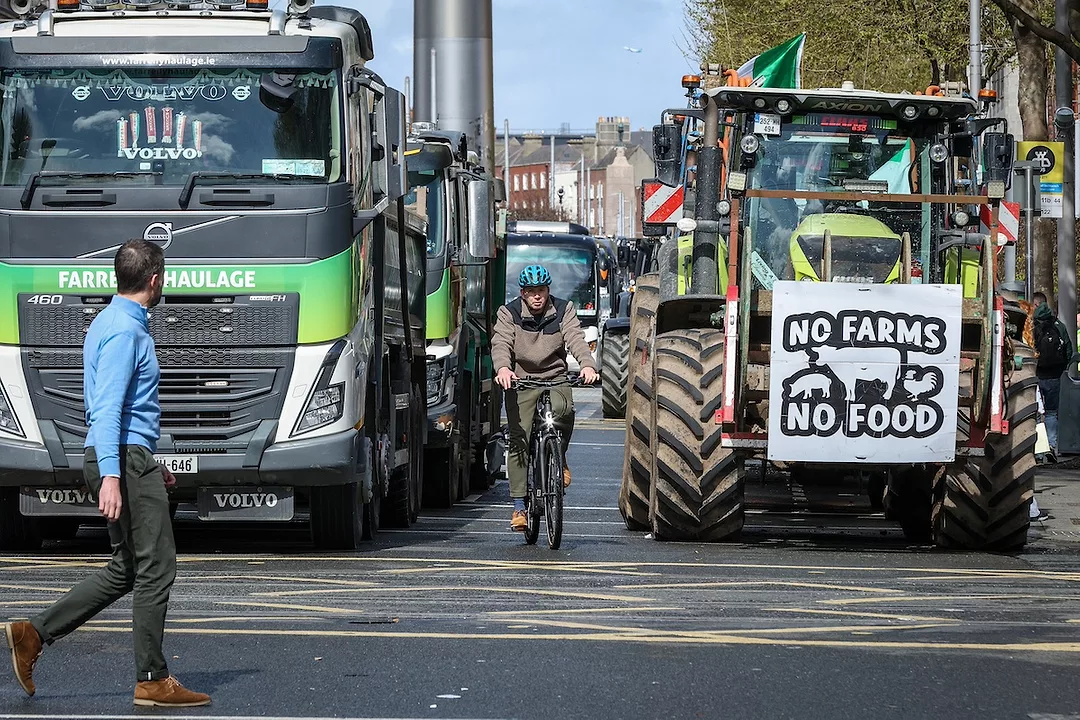 A tractor with a banner that reads "No Farms, No Food" and a green semi-truck block a busy road