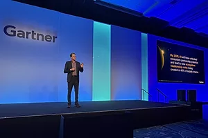 A man in a suit standing on a stage in front of a large screen that reads "GARTNER"