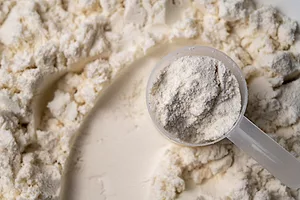 A pile of white protein powder with a small plastic scoop on top